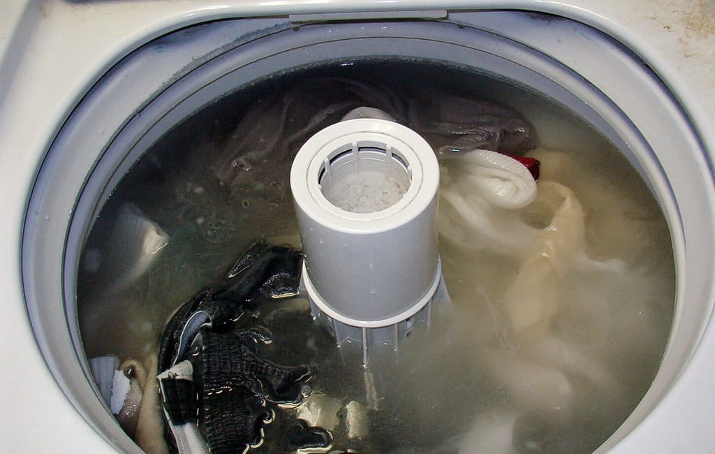 Top view of a washing machine filled with water and various clothes during a wash cycle.