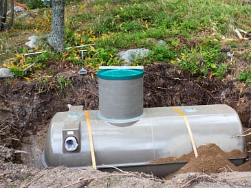 A newly installed septic tank partially buried in the ground with a green lid on top.