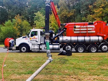 A large septic tank service truck with a hose connected to a septic tank on the ground.