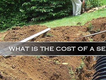 Person digging a trench for a septic system installation with black septic tank components visible.