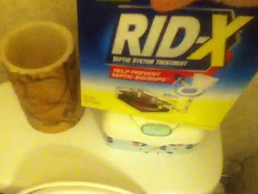 Hand holding a box of RID-X septic system treatment above a toilet tank.