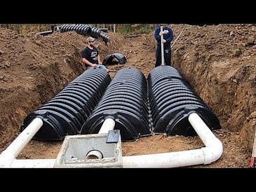 Two workers installing infiltrator chamber septic tanks in a trench.