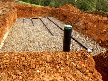 Excavated area showing a septic system with gravel and pipes in place.
