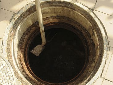 Open septic tank access point with a shovel resting on the edge, showing dark contents inside.