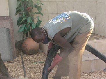 A man wearing a tank top and gloves handling a large black hose in a maintenance area.