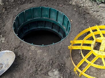 Open septic tank access point with a green circular structure and yellow cover nearby.