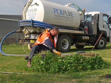 Technician in safety gear working on a liquid waste management system beside a service truck.
