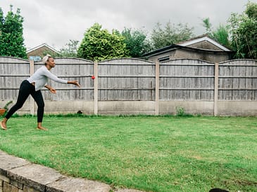 An adult throwing a red ball to a child in a backyard with a wooden fence.