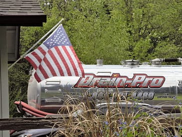 Silver septic service truck with Drain-Pro branding and an American flag attached.