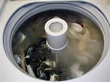 Top view of a washing machine filled with water and various clothes during a wash cycle.