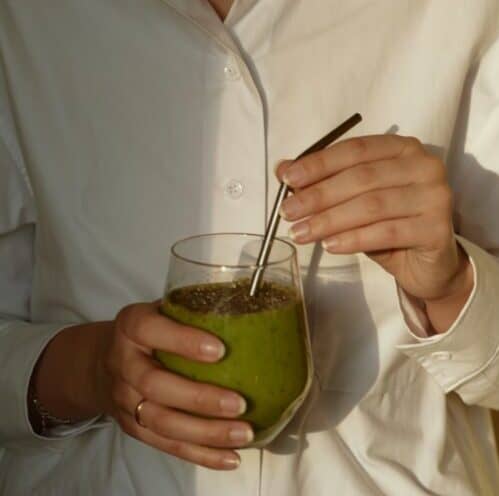 person in white button up shirt holding clear drinking glass with green liquid