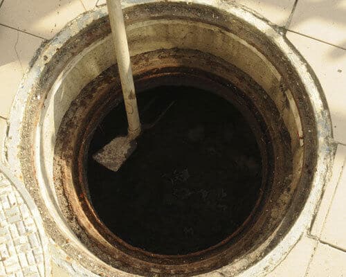 Open septic tank access point with a shovel resting on the edge, showing dark contents inside.