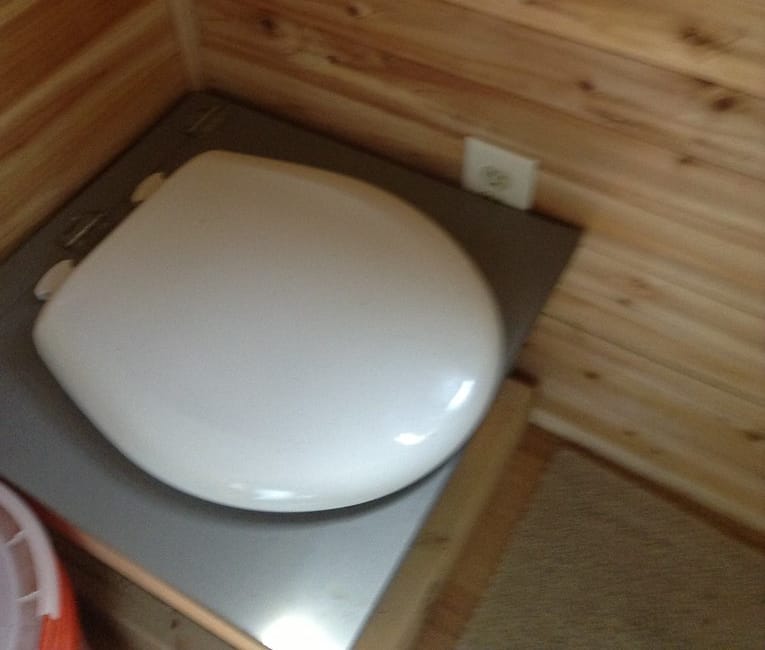 White toilet positioned on a wooden platform in a rustic interior setting.