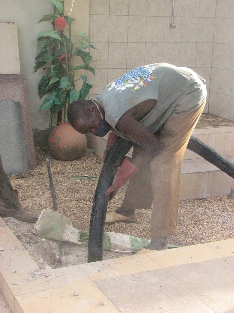 A man wearing a tank top and gloves handling a large black hose in a maintenance area.