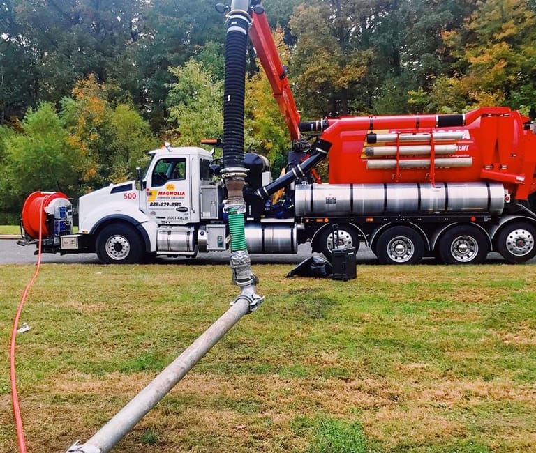 A large septic tank service truck with a hose connected to a septic tank on the ground.