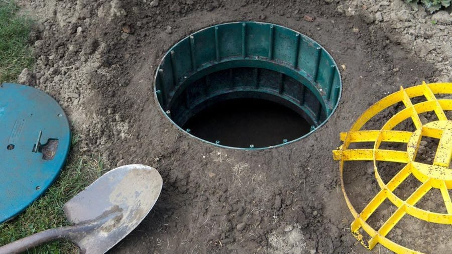 Open septic tank access point with a green circular structure and yellow cover nearby.